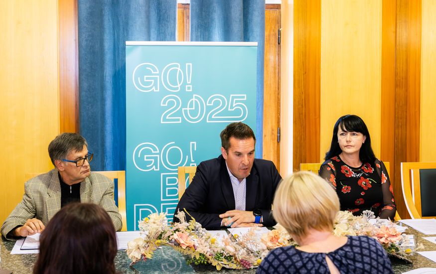 Župan med govorom za mizo na novinarski konferenci. Zraven sta še Marinka Saksida (na desni) in Marjan Zahar (na levi).