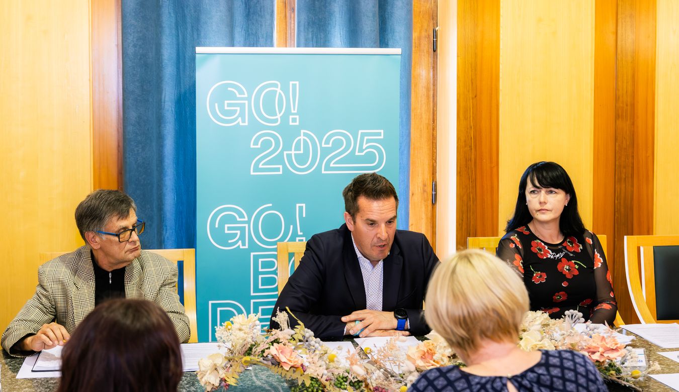 Župan med govorom za mizo na novinarski konferenci. Zraven sta še Marinka Saksida (na desni) in Marjan Zahar (na levi).